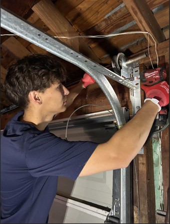 Technician repairing garage door cables with a power tool