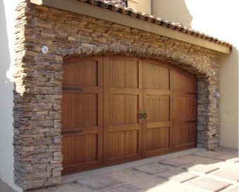 Honey-toned custom wood garage door set in a stone archway