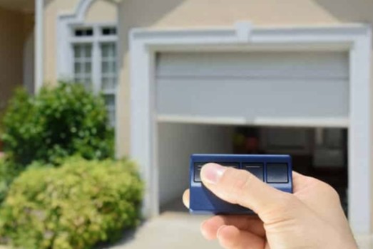 Hand pressing a garage door remote with the garage door open in the background